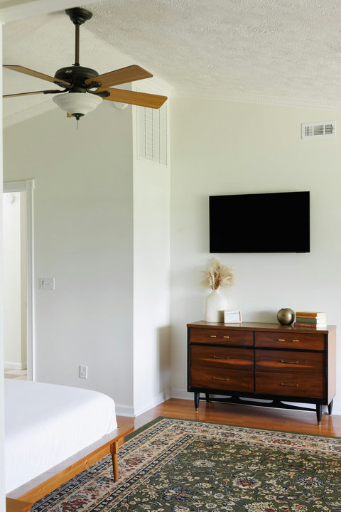Bright minimalist bedroom with TV, ceiling fan, and warm wood accents