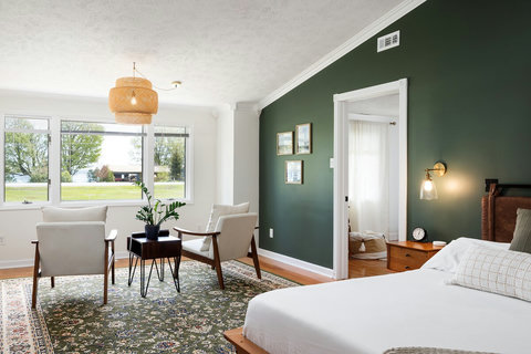 Bright bedroom retreat with cozy seating, large windows, and elegant green accents