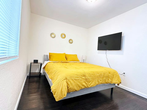 Bedroom with queen size bed, alarm clock, two nightstands, lamp, smart TV