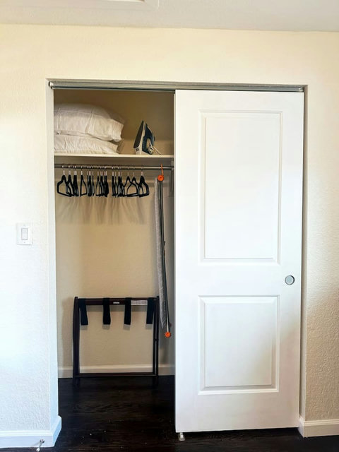Bedroom closet with hangers for your clothes, iron and ironing board, extra pillows, storage