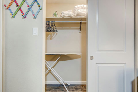 Bedroom closet with plenty of storage space, hangers, an iron and ironing board, and extra sheets and pillows