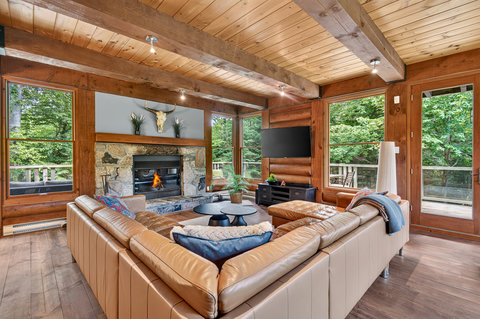 Cozy wood-beamed living room with stone fireplace and forest views