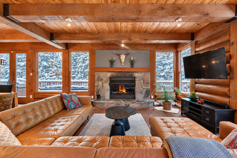Cozy log cabin lounge with stone fireplace and snowy woodland views