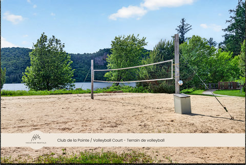 Sandy lakeside volleyball court with scenic forest views