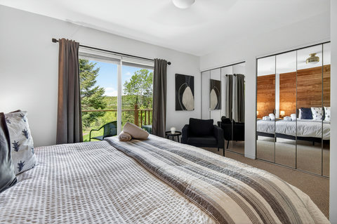 Bright bedroom with private balcony, mirrored closets, and treetop views