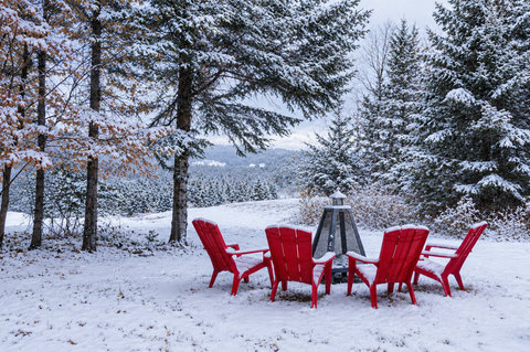 Snowy fire pit retreat with red Adirondack chairs and serene forest views