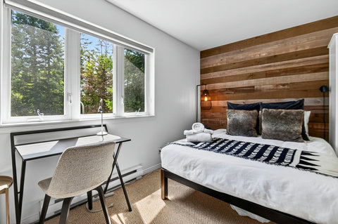 Bright cozy bedroom with wood accent wall, desk, and serene garden views