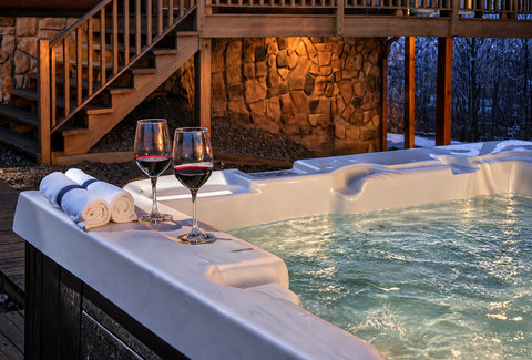 Private hot tub with wine, warm lighting, and cozy cabin charm