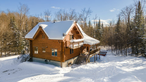Cozy log cabin retreat with wraparound deck in a snowy forest