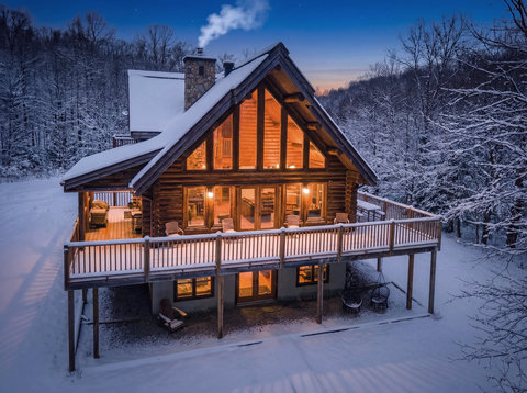 Cozy log cabin with wraparound deck in a serene snowy mountain setting