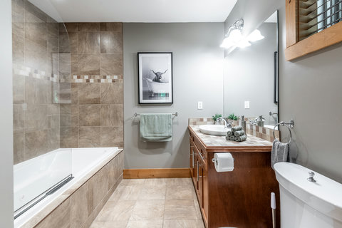 Bright spa-style bathroom with tiled tub, large vanity, and warm wood accents