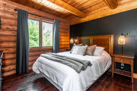 Cozy log cabin bedroom with plush bed, warm wood interiors, and forest views
