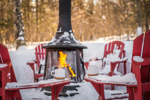 Cozy winter fire pit with red Adirondack chairs in a snowy forest