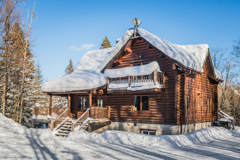 Cozy snow-covered log cabin with porch, balcony, and serene wooded setting