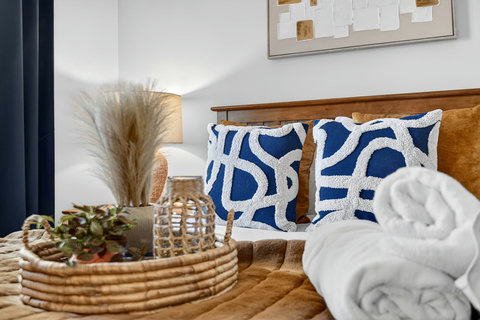 Warm, modern bedroom with bold pillows, rattan accents, and fresh towels.