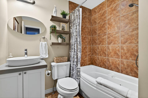 Cozy bath with jetted tub, vessel sink, and warm tile shower.