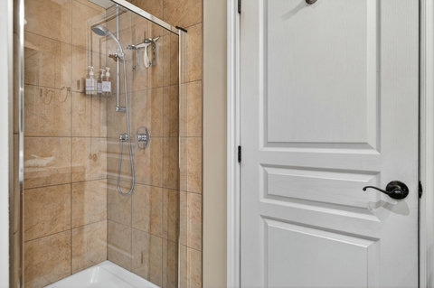 Sparkling tiled shower with glass door, rain wand, and stocked dispensers.