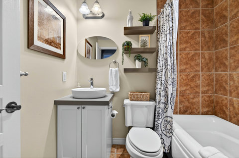 Warm tiled bath with vessel sink, decor shelves, and tub-shower.