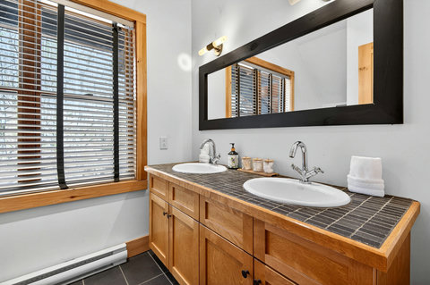 Bright bath with double sinks, warm wood, and sleek black accents