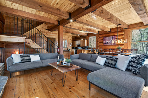 Rustic-chic cabin great room with XL sofa, dining & forest views