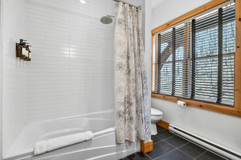 Bright bath with rainfall shower, slate floors, and wooded-view window