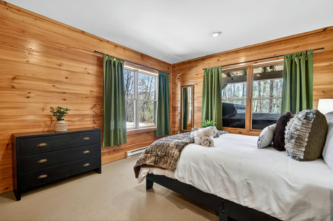 Cozy wood-paneled bedroom with forest views and hot tub just outside