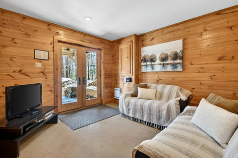 Cozy wood-paneled lounge with French doors to a serene forest patio