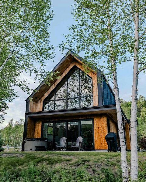 LumiHaus opens directly onto the forest, with soaring floor-to-ceiling windows that blur the line between indoors and nature. This view is taken from the forest, looking back at the chalet’s stunning glass front.