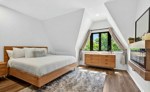 Bright modern bedroom with vaulted ceilings, fireplace, and treetop views