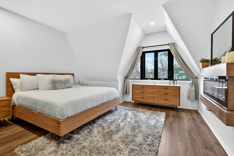 Bright vaulted bedroom with fireplace, TV, and peaceful treetop views