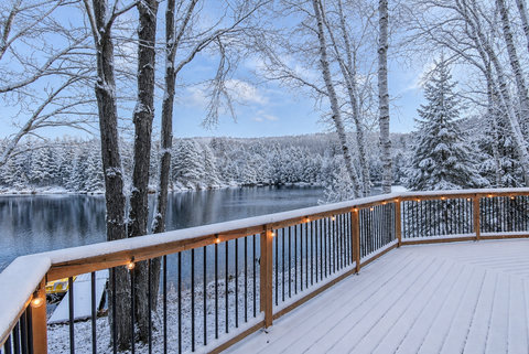Snowy lakefront deck with twinkle lights and peaceful forest views