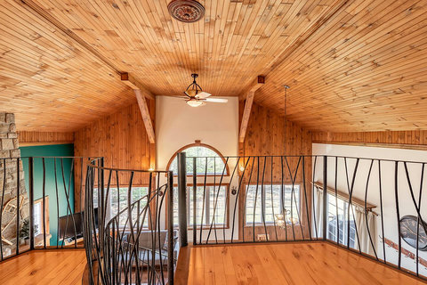 Mezzanine view of living room with its abundant fenestration and lighting and its cathedral roof and fireplace