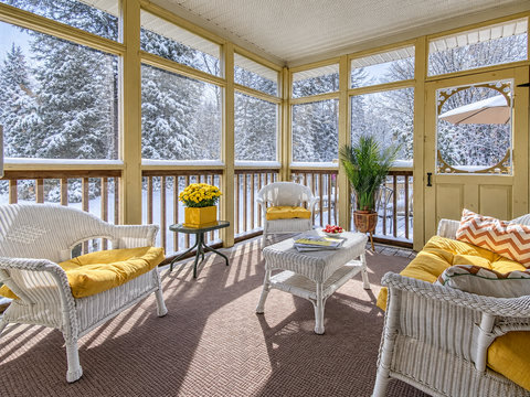 Sunny screened porch with cozy seating and stunning snowy forest views