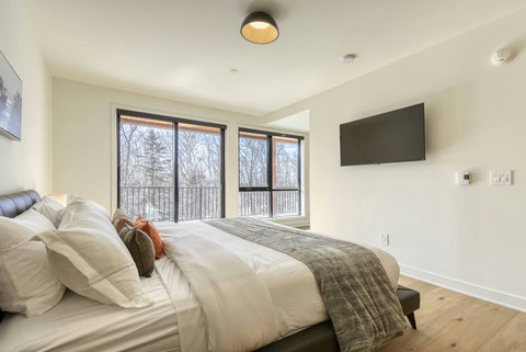 Bright modern bedroom with forest views and a wall-mounted TV