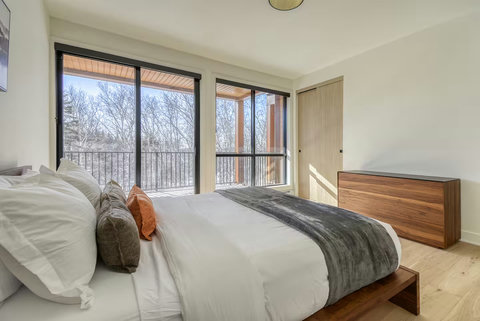 Sunlit bedroom with balcony access and peaceful treetop views