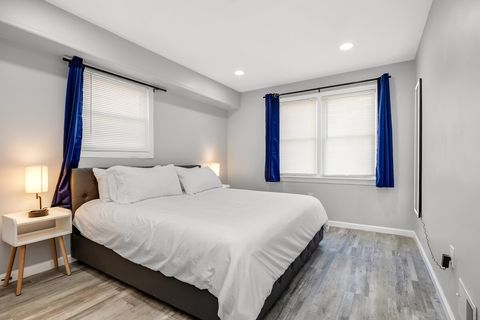 Hotel-quality king bed with crisp white linens, blackout-ready blue curtains, USB nightstands on both sides, and an LED body mirror — one of three king bedrooms in this duplex.
