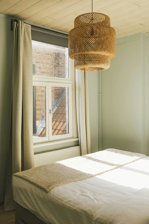 Serene double bedroom with rattan pendant light and morning sun over historic rooftops