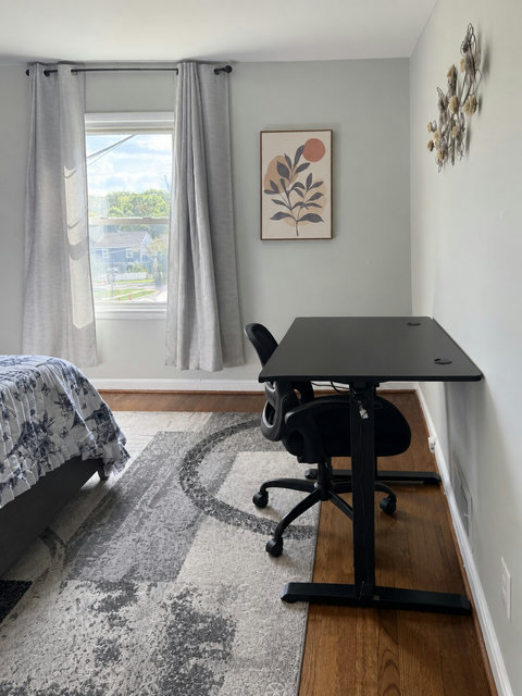 Bedroom workspace with a height-adjustable desk and office chair. Photo enhanced for brightness and alignment.