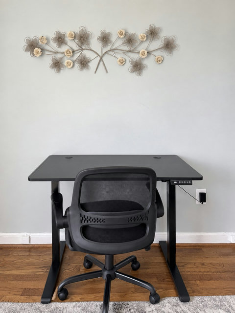 Dedicated work area within a bedroom, with a height-adjustable desk and office chair. Photo enhanced for brightness and alignment.