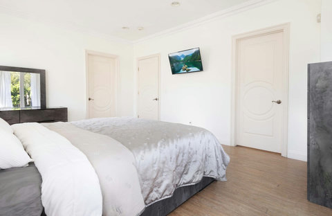 Wide perspective of the bedroom showing the open layout, mounted TV, and multiple entry points including the ensuite area and hallway.