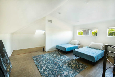 Bright loft style guest room with two twin beds, a workspace, and plenty of natural light from surrounding windows.