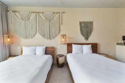 Two cozy beds with natural wood frames, boho macramé wall art, and warm pendant lighting—perfect for a restful night's sleep.