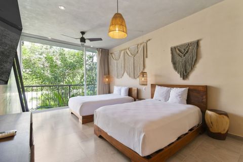 Bright bedroom with two cozy beds, boho macramé decor, a ceiling fan, and floor-to-ceiling windows with lush jungle views.