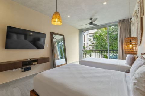 Boho-style bedroom with two comfy beds, smart TV, full-length mirror, ceiling fan, and large windows opening to a private balcony with lush views.