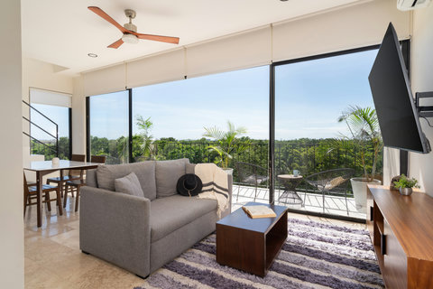 Relax in this beautifully designed living room featuring cozy seating, warm decor, and expansive windows that fill the space with natural light—perfect for quiet mornings or sunset views.
