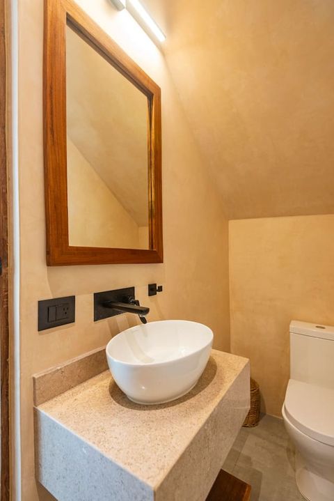 Stylish half bathroom featuring a stone countertop with a vessel sink, a wooden-framed mirror, and sleek black fixtures. Warm lighting and natural tones create a cozy, modern feel.