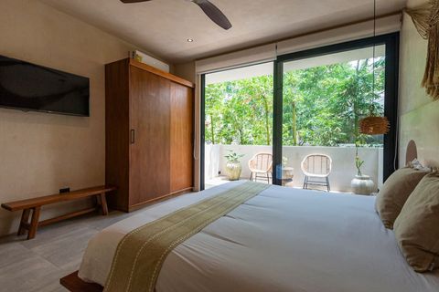 Elegant bedroom with a sliding glass door leading to a private balcony. Features a wall-mounted TV, king size bed,  wooden wardrobe, and boho-chic decor.