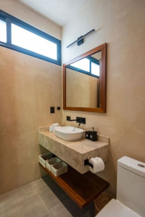 Stylish half bathroom featuring a stone countertop with a vessel sink, a wooden-framed mirror, and sleek black fixtures. Warm lighting and natural tones create a cozy, modern feel.