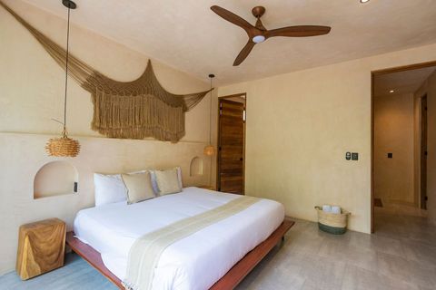 Modern bohemian bedroom featuring a king-size bed, handcrafted wooden furniture, and soft neutral tones. Large windows invite natural light and a fresh breeze.