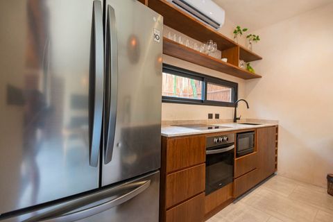 Modern minimalist kitchen with a stainless steel fridge, sleek wooden cabinets, open shelves, and an air conditioning unit. A large window adds natural light and a cozy touch.